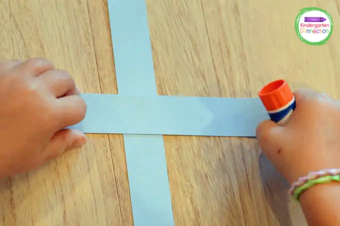 To begin, the students will glue two strips of blue paper together in the shape of a cross.