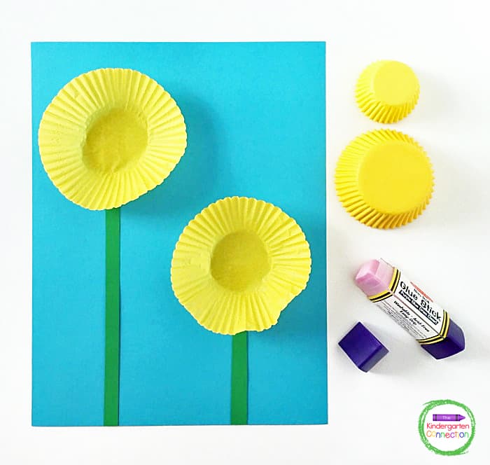 Glue the green paper strips and large cupcake liners to the blue cardstock to create your flowers and stems.