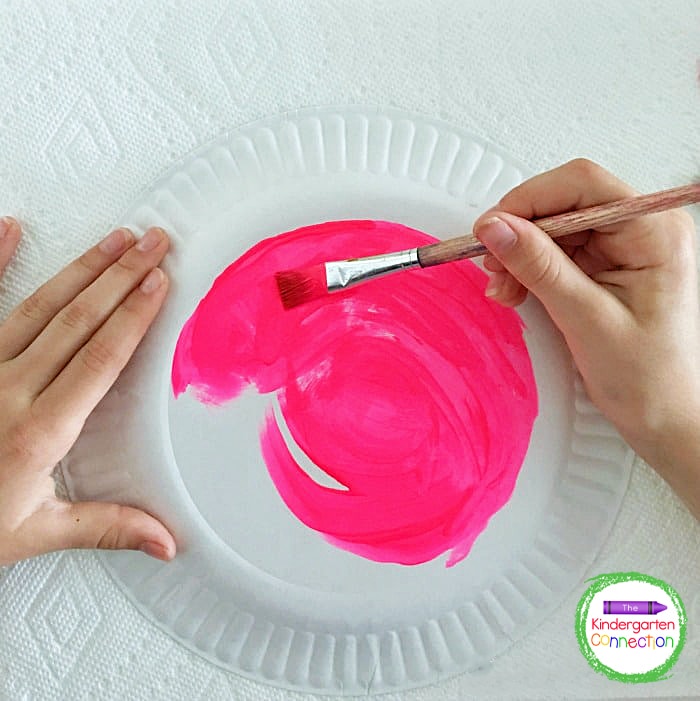 Begin by painting the center of the paper plate with pink tempera paint.