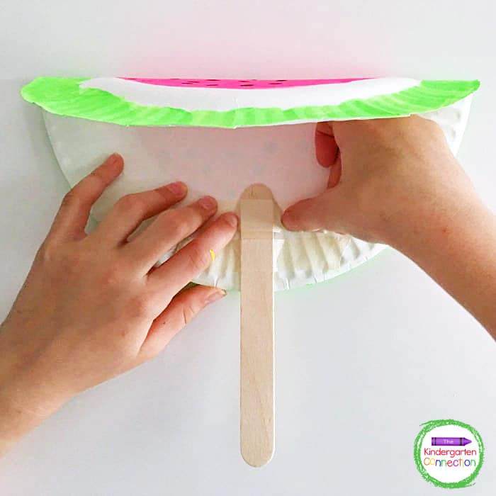 Open the plate and use masking tape to attach a large craft stick for the handle of the fan.