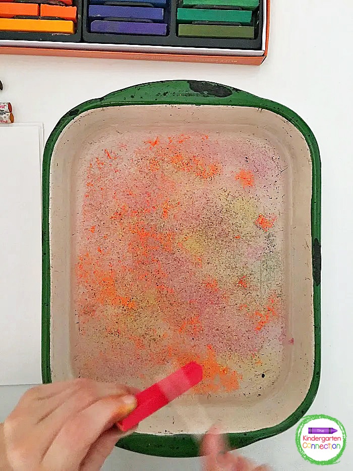 Continue scraping chalk pastels around the entire dish of water with several other colors.
