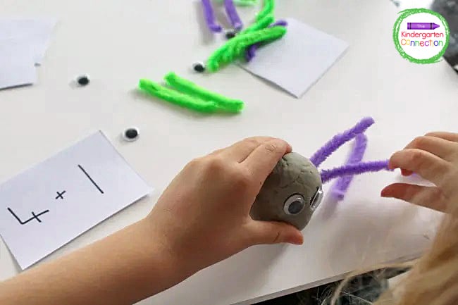 Cut two different colors of pipe cleaners into small pieces to use for the spiders' legs and write the addition problems on small pieces of paper.