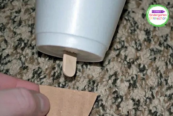 Cut a small half-moon out of the leftover cardboard. We will attach this to the bottom of our popsicle stick so it doesn’t slide through the hole.