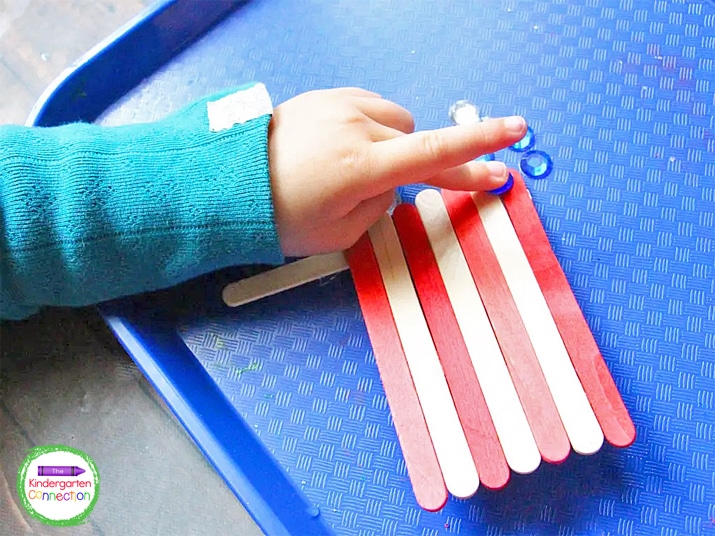 Add a second popsicle stick to the side of the flag for an optional "flag pole" and glue the gems on for the stars.