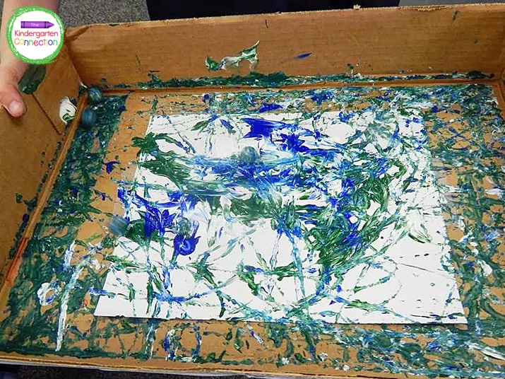 Cover the paper with blue, green, and white paint and start rolling marbles in the tray to spread the paint.